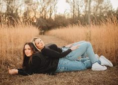 two young women laying on the ground in tall grass with their arms around each other