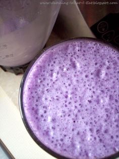 a purple drink sitting on top of a counter next to a blender filled with liquid