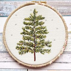 a cross stitch christmas tree is hanging on a wooden hoop with red and white thread