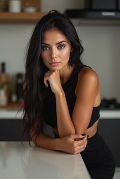 a beautiful young woman sitting at a kitchen counter posing for the camera with her hands on her chin