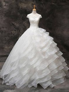 a white wedding dress with ruffles on the skirt and neckline is displayed in front of a dark background