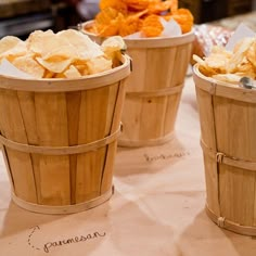 three wooden buckets filled with chips sitting on top of a table next to other food