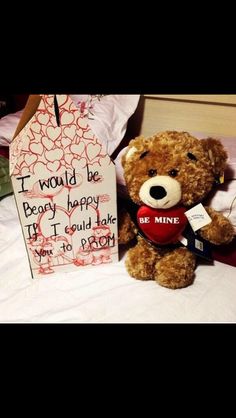 a brown teddy bear sitting on top of a bed next to a valentine's day sign