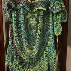 a crocheted green and purple shirt hanging on a wooden frame in front of a mirror