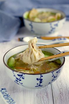 two bowls filled with soup and chopsticks on top of a white wooden table