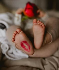 a person with red lipstick on their feet laying down next to a flower and a rose