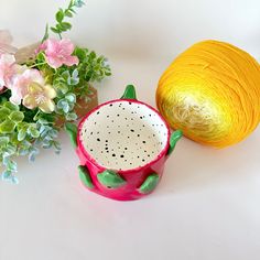 a crochet pot next to a yellow ball of yarn and some pink flowers