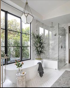 a large white bathtub sitting next to a window in a bathroom with a potted plant