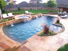 a backyard pool with a waterfall and seating area in the center, surrounded by lawn furniture