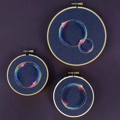 three embroidery hoops with circular designs on them, hanging from the wall in front of a purple background