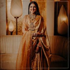 a woman in a gold sari standing next to a couch with a lamp on it