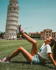 a woman laying on the ground in front of a leaning tower with her legs spread out