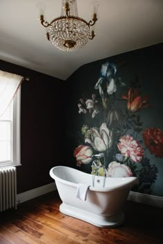 a bath tub sitting next to a chandelier in a room with flowers on the wall