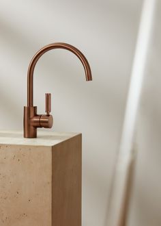 a copper faucet sitting on top of a block of concrete next to a white wall