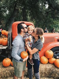 a man, woman and child standing in front of an orange truck with pumpkins