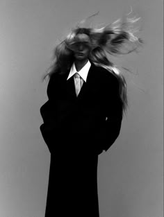 a woman with her hair blowing in the wind wearing a black coat and white shirt