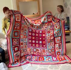 two women standing next to each other holding up a colorful blanket in front of them