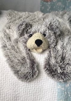 a teddy bear laying on top of a bed covered in gray fur and a white blanket