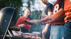 two men grilling hot dogs and sausages on an outdoor grill