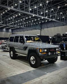 an suv is on display in a showroom with other vehicles and people looking at it