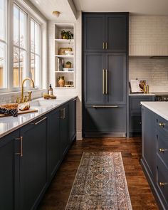 a kitchen with dark blue cabinets and gold pulls on the doors, along with an area rug