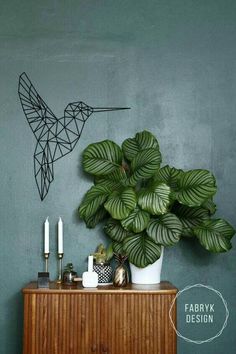 a green plant sitting on top of a wooden cabinet next to a bird shaped wire sculpture