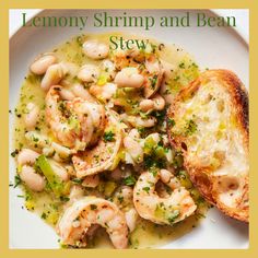 a white plate topped with shrimp and bean stew next to a piece of toasted bread