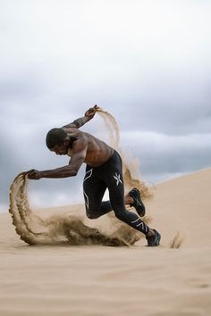 a man is running in the sand with his foot on an object that looks like a tire