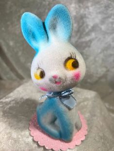 a blue and white rabbit figurine sitting on top of a gray cloth covered surface