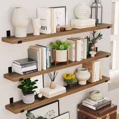 three wooden shelves with books, plants and pictures on them next to a window in a living room