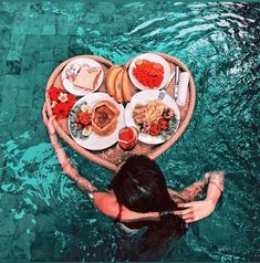 a woman is floating in the water with food on her heart shaped plate and plates