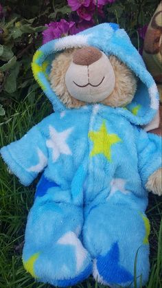 a teddy bear is laying in the grass wearing a blue outfit with stars on it