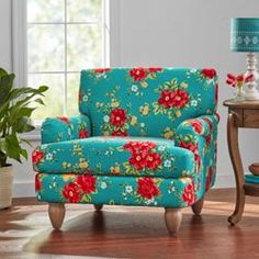 a blue chair with red flowers on it next to a table and potted plant