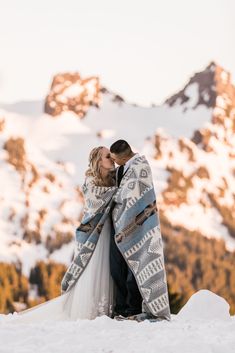 a bride and groom standing in the snow under a blanket