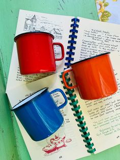 two red and blue mugs sitting on top of an open notebook