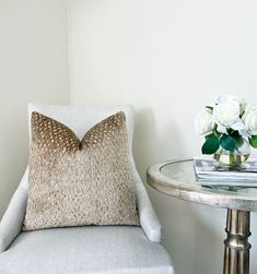 a white chair with a pillow on top of it next to a table and flowers