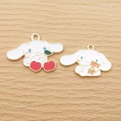 two charms sitting next to each other on top of a wooden surface, one has a dog and the other has an apple