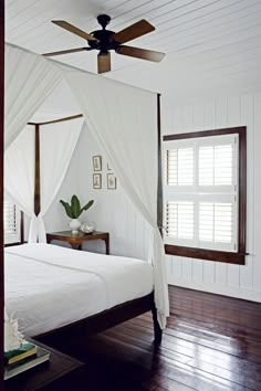 a white bed sitting in a bedroom on top of a wooden floor next to a window