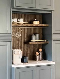 a kitchen with gray cabinets and white counter tops in front of grey cupboards that have wooden shelves above them