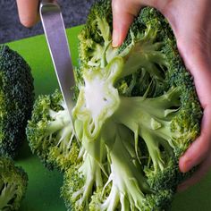 someone cutting up broccoli on a green cutting board