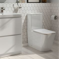 a white toilet sitting next to a sink in a bathroom with hexagonal tiles on the walls