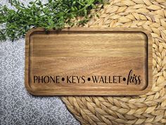 a wooden sign that says phone keys wallets on it next to a basket with some plants