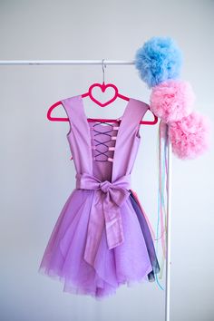 a pink and purple dress hanging on a clothes line with two pom poms