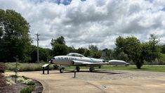 an airplane is parked on the cement near some trees and bushes with clouds in the background