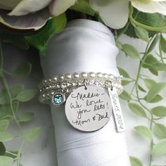 a stack of white napkins with personalized bracelets on them and flowers in the background