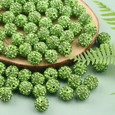 a wooden spoon filled with green beads next to a fern leaf and some leaves on the table