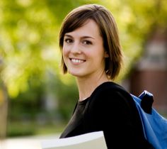 a woman with a book in her hand smiles at the camera while standing outside on a sunny day