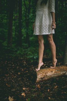 black and white photograph of woman standing on log in the woods with trees behind her