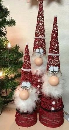 three red and white gnomes are sitting in front of a christmas tree