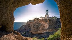 the light house is visible through an opening in the rock